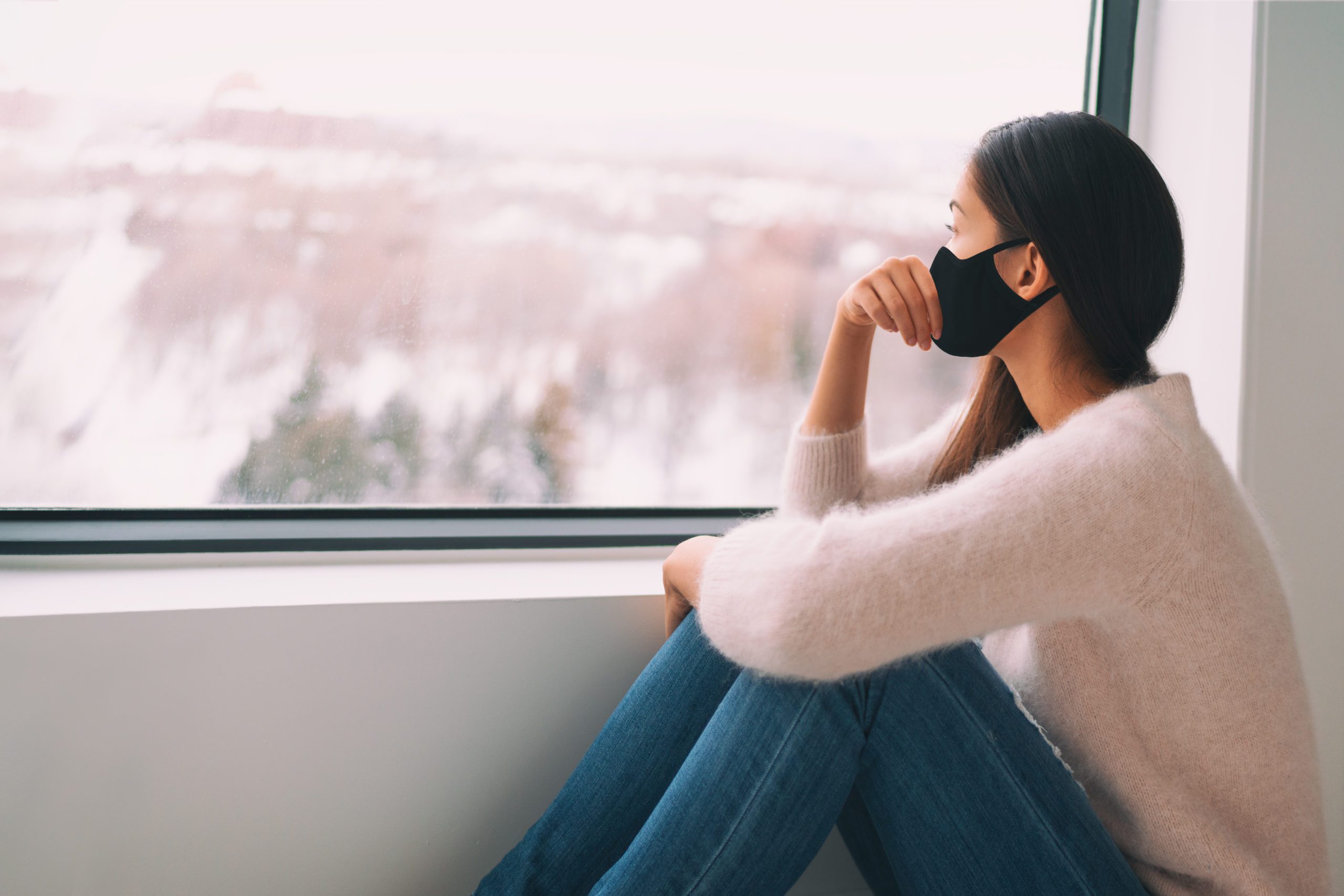 woman wearing a face covering looking out of a window