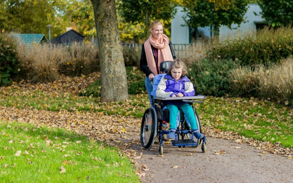 woman pushing girl in a wheelchair in a park