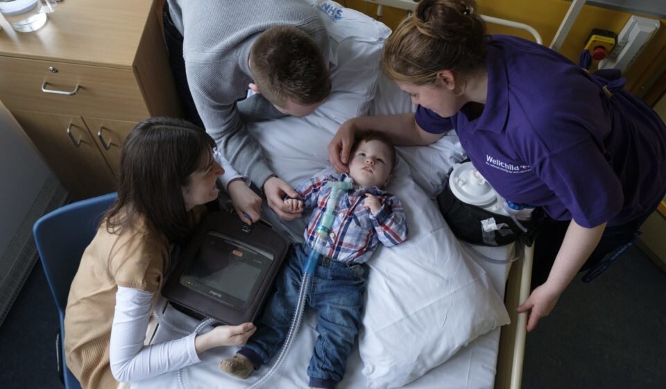 parents with child on a hospital bed with ventilator, with their WellChild Nurse