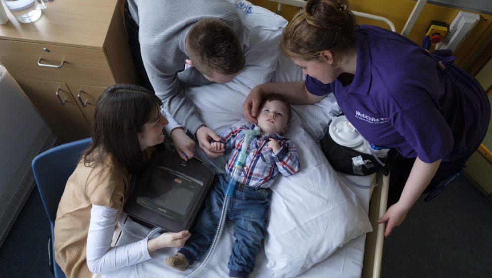 parents with child on a hospital bed with ventilator, with their WellChild Nurse