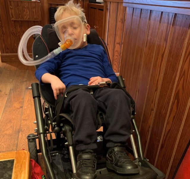 Joshua in his wheelchair using breathing equipment