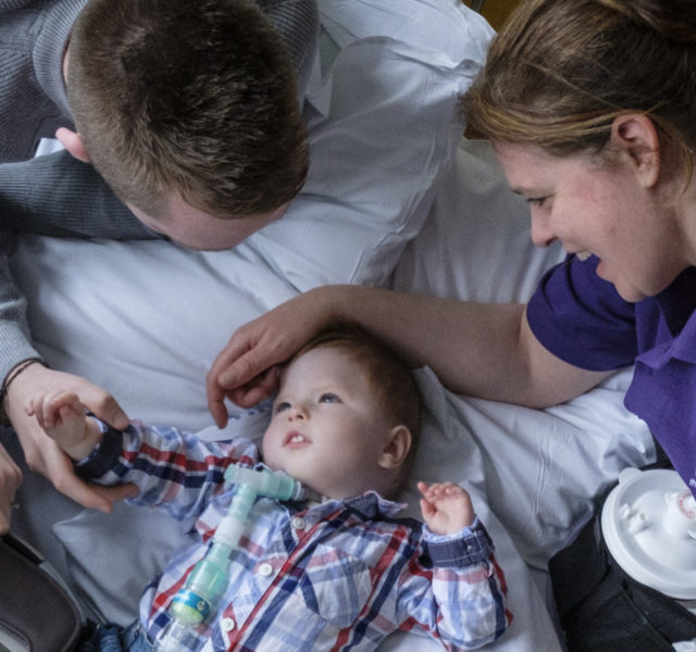 Ariel shot of a young boy lying in a hospital bed with his parents and WellChild Nurse looking over him.