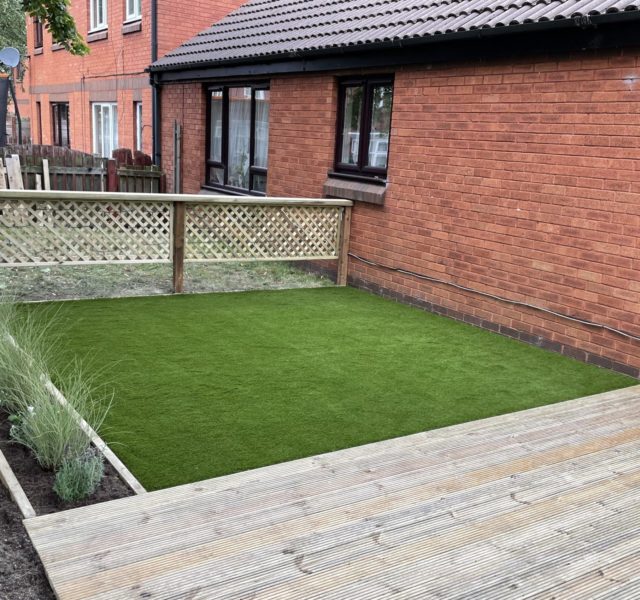 Accessible garden with artificial grass, fencing and a sensory water feature.