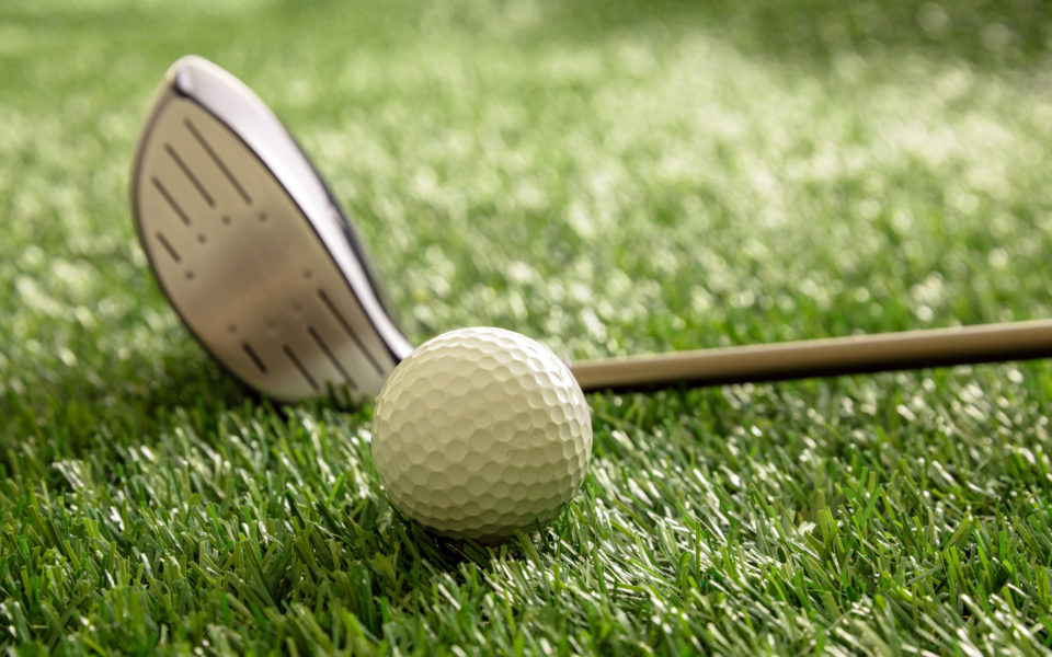 Golf stick and ball on green grass golf course, close up view.
