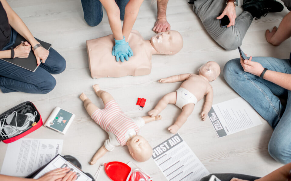 Group of people learning how to make first aid heart compressions with dummies during the training indoors