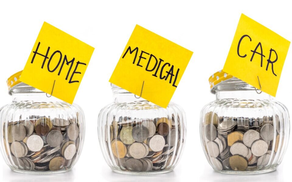 Picture of 5 jars filled with coins. Each Jar has a post-it note attached. One says Save, Ones says Home, One says Medical, One says Car, One says travel